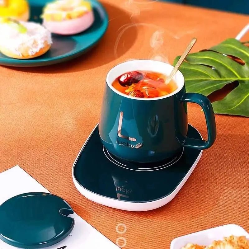 Electric coffee warmer with a steaming cup of tea on a stylish table next to colorful desserts.
